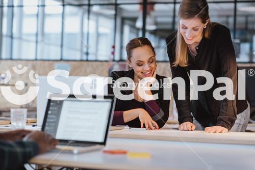 Two Professionals Collaborating On A Creative Project At The Office. Diverse Team Reviewing A Document With Smiles.